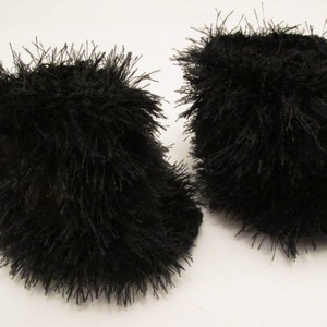 Puede incluir: Un par de pantuflas de felpa negra. Las pantuflas están hechas de un material suave y esponjoso y tienen una forma simple y redondeada.