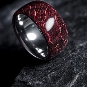 May include: A ring featuring a polished dark burgundy outer band with a distinct, light-coloured veined pattern resembling marble or wood grain. The interior of the band is made of a smooth, reflective silver-toned metal with a high-gloss finish.