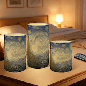 以下が含まれることがあります： ゴッホの「星月夜」が描かれた、3つの円筒形LEDキャンドルのセット。高さの異なるキャンドルが、リモコンと一緒にテーブルに置かれています。この作品は、星と村のある渦巻く夜空を描いています。