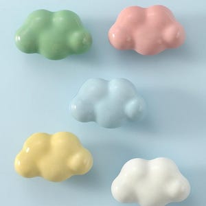 May include: A white ceramic mug with a black handle and the text "But First, Coffee" in a bold, black font. The mug is set against a blurred background. The mug appears to be approximately 10 cm tall.