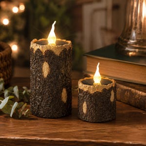 May include: Two cylindrical LED candles with a textured dark brown bark exterior and light tan wood-grain accents. Each candle features a glowing, flame-shaped light bulb at the top, mimicking the appearance of a natural tree log with bark.