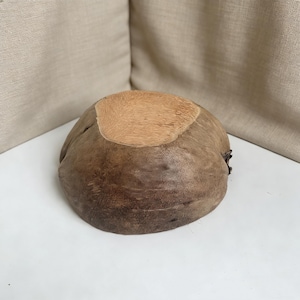 May include: A handcrafted, wooden bowl with a natural, organic shape. The bowl features a light brown, textured interior and a darker, weathered exterior. The bowl is likely made from a coconut shell and is suitable for decorative or functional use.
