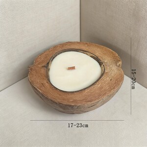 May include: A coconut shell candle with a white wax interior and a wooden wick. The candle is nestled in a natural coconut shell, measuring approximately 17-23 cm in length and 15-20 cm in height. The candle is a natural home decor item.