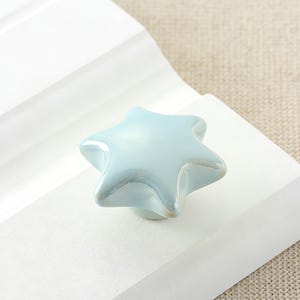 Könnte beinhalten: Eine weiße Keramiktasse mit schwarzem Henkel und dem Text "But First, Coffee" in fetter, schwarzer Schrift. Die Tasse steht vor einem verschwommenen Hintergrund, der eine gemütliche Umgebung suggeriert.