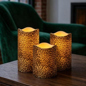 Op de afbeelding: Drie cilindervormige LED-kaarsen met een bruin en zwart luipaardpatroon. Elke kaars heeft een golvende, onregelmatige bovenrand en straalt een warm licht van binnenuit uit, wat zorgt voor een zachte verlichting over het textuurrijke oppervlak.