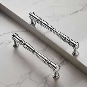 May include: Two polished chrome cabinet pulls featuring a cylindrical design with rounded ends and decorative ridges. Each handle is engraved with the name Jones in a cursive script, accompanied by a delicate leaf motif on the metal surface.