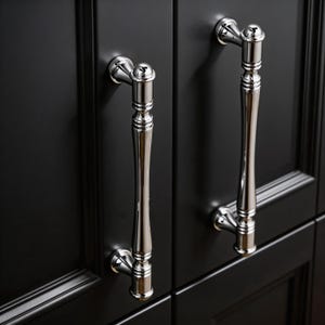Peut inclure: Gros plan sur deux poignées de placard chromées polies contre une porte de placard noire. Les poignées ont un design classique et élégant avec une forme incurvée et allongée et des détails décoratifs. Les poignées sont montées sur une surface sombre et à panneaux.