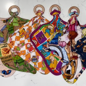 May include: A collection of six baby security blankets with wooden ring attachments. Each blanket features a different colorful cartoon character print, including Sesame Street, Rugrats, and Toy Story designs.