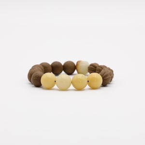 May include: A beaded bracelet featuring a mix of round and textured beads in shades of brown and cream. The bracelet has a variety of bead sizes and textures, creating a unique and eye-catching design. The bracelet is displayed on a white background.