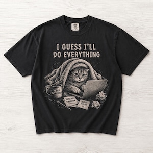 Peut inclure: Un t-shirt noir à manches courtes avec un motif représentant un chat enveloppé dans une couverture devant un ordinateur portable. Le texte indique I GUESS I'LL DO EVERYTHING. On voit un mug TEAM OVERWORKED, un stylo et deux notes DEADLINE: TOMORROW et NOBODY REPLIED.