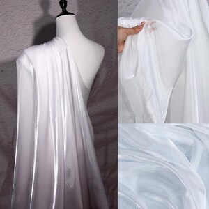 May include: White fabric draped over a mannequin, with a shiny, reflective quality. The fabric appears to be lightweight and flowing, with soft folds and a subtle gradient. The image also shows close-ups of the fabric's texture and transparency.