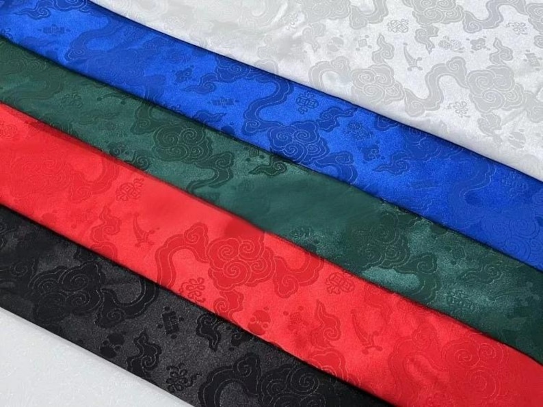 May include: Five strips of satin fabric arranged diagonally in white, blue, green, red, and black. Each strip features a tonal jacquard pattern of stylized clouds and traditional geometric motifs woven into the smooth, reflective material.