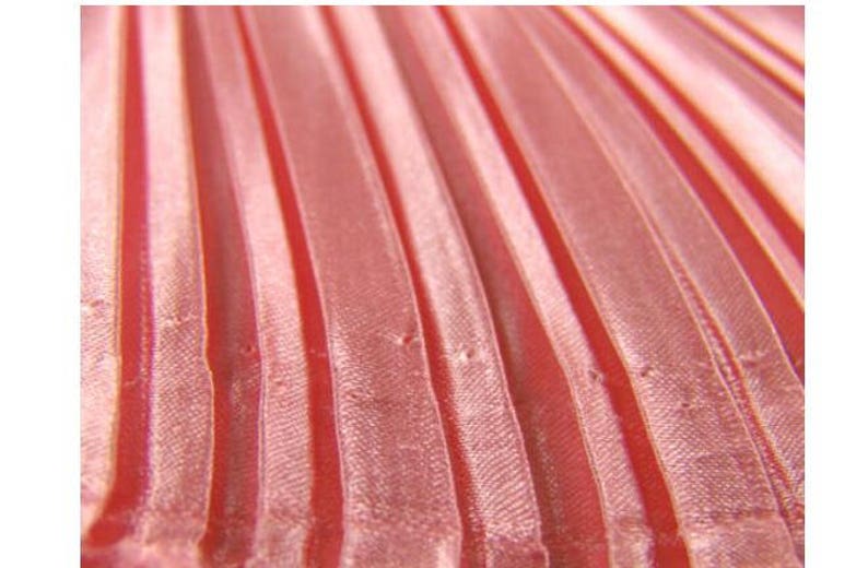 May include: Close-up of a red fabric with a pleated texture. The fabric has a subtle sheen and a slightly wrinkled appearance.
