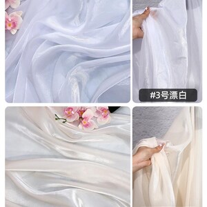 May include: White and off-white sheer fabric with a silky sheen. The fabric is draped and folded, creating soft waves. Pink orchids are placed on the fabric. The text "#3" and "#4" are visible.
