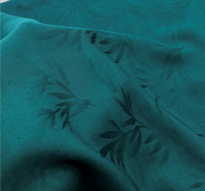 May include: Teal fabric with a subtle embossed leaf pattern. The fabric has a smooth, silky texture.