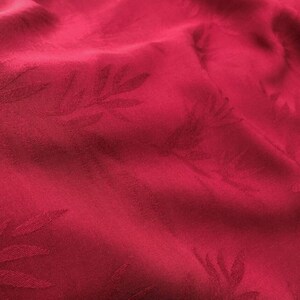 May include: Red fabric with a subtle embossed pattern of leaves. The fabric has a smooth, silky texture.