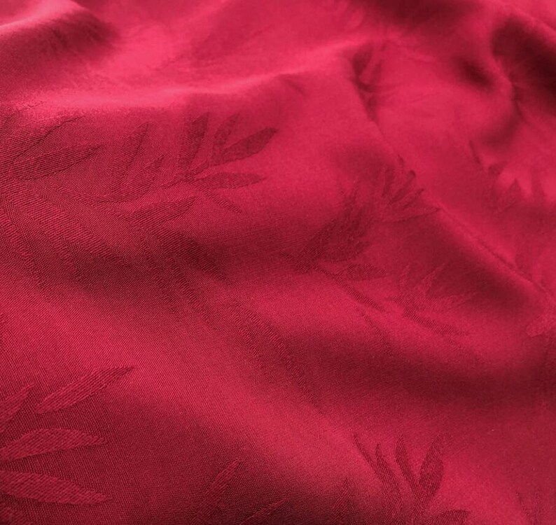 May include: Red fabric with a subtle embossed pattern of leaves. The fabric has a smooth, silky texture.