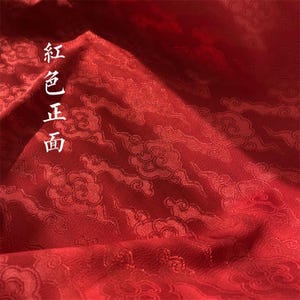 May include: A deep red fabric featuring a repeating woven pattern of stylized clouds. The surface has a subtle sheen and includes the vertical Chinese characters 紅色正面 printed in white on the left side of the textile material.