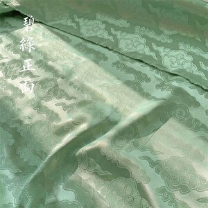 May include: A light green fabric featuring a woven pattern of stylized clouds. The material has a subtle sheen and includes white Chinese characters printed on the upper left side, which read 碧綠正面, indicating the front side of the green fabric.