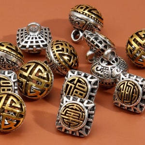 May include: A collection of 10 silver and gold decorative buttons with intricate Chinese character designs. The buttons are round and square in shape and have a textured finish.