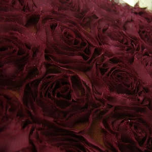 May include: Burgundy red fabric with a 3D rose pattern. The fabric is made of a soft, delicate material and has a subtle sheen.