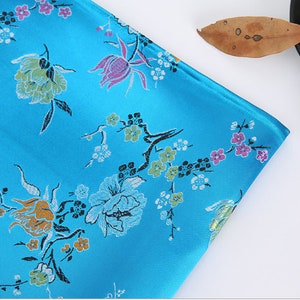 May include: A blue fabric with a floral pattern. The fabric has a satin finish and features a variety of flowers in shades of pink, yellow, and green.