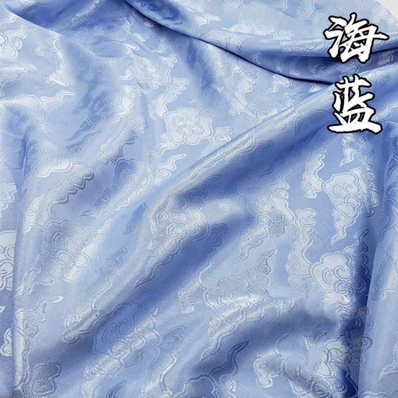 May include: A light blue fabric featuring a repeating tonal pattern of stylized clouds. The material has a smooth, satin-like sheen with visible folds and drapes. The Chinese characters 海蓝 are printed in the upper right corner in black ink.