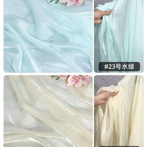 May include: A collage of sheer fabric samples in shades of light blue and cream, with a glossy finish. The fabric is draped and folded, with a sprig of pink flowers in the background. The text "#23" and "#24" is visible.