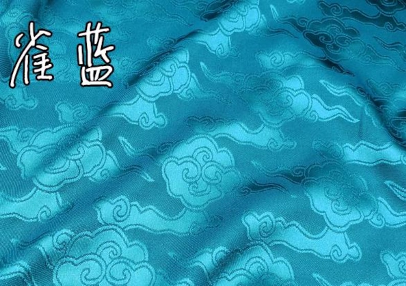 May include: A vibrant turquoise fabric featuring a repeating woven pattern of stylized clouds. The material has a subtle sheen and includes the Chinese characters 雀蓝 in the upper left corner, which translate to peacock blue.