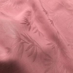 May include: A close-up of a pink fabric with a subtle embossed leaf pattern. The fabric has a soft, smooth texture.