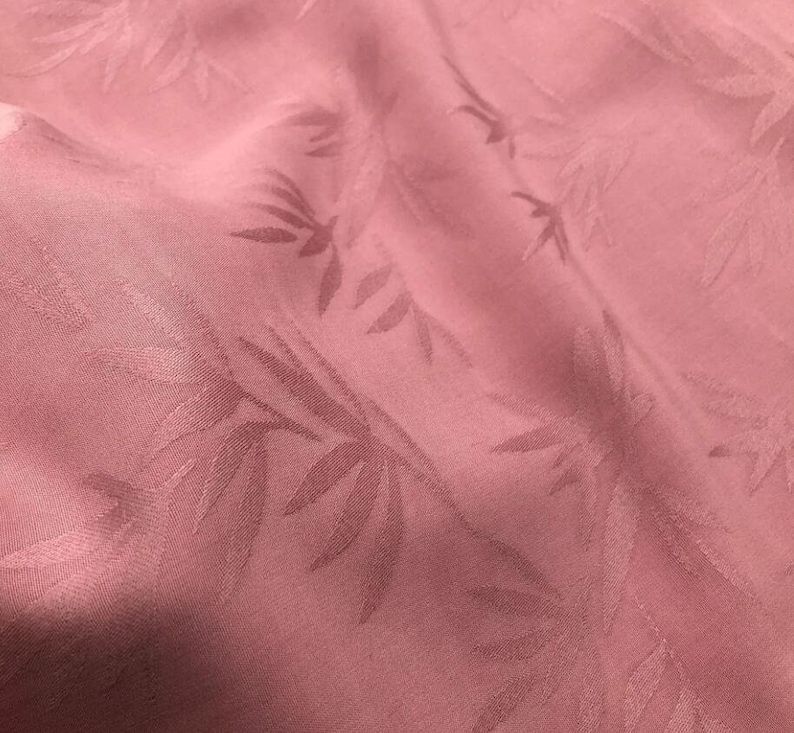 May include: A close-up of a pink fabric with a subtle embossed leaf pattern. The fabric has a soft, smooth texture.