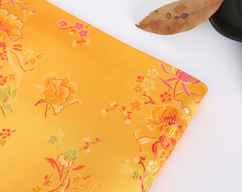 May include: A yellow fabric with a floral pattern. The fabric features pink, red, and green flowers on a yellow background.