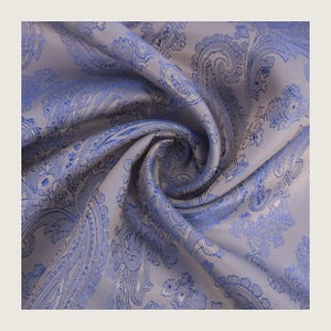 May include: Close-up of a folded fabric with a paisley pattern. The fabric is a light gray color with a blue paisley design. The fabric is soft and has a slight sheen.