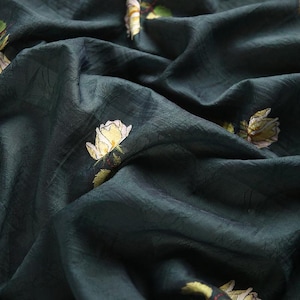 Pu&ograve; includere: Tessuto verde scuro con una trama sottile e rose gialle ricamate con foglie verdi. Il tessuto ha una leggera lucentezza ed &egrave; drappeggiato, creando pieghe e ombre morbide.