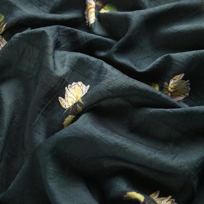 Pu&ograve; includere: Tessuto verde scuro con una trama sottile e rose gialle ricamate con foglie verdi. Il tessuto ha una leggera lucentezza ed &egrave; drappeggiato, creando pieghe e ombre morbide.