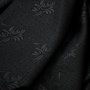 May include: Black fabric with a repeating pattern of stylized flowers and geometric designs.