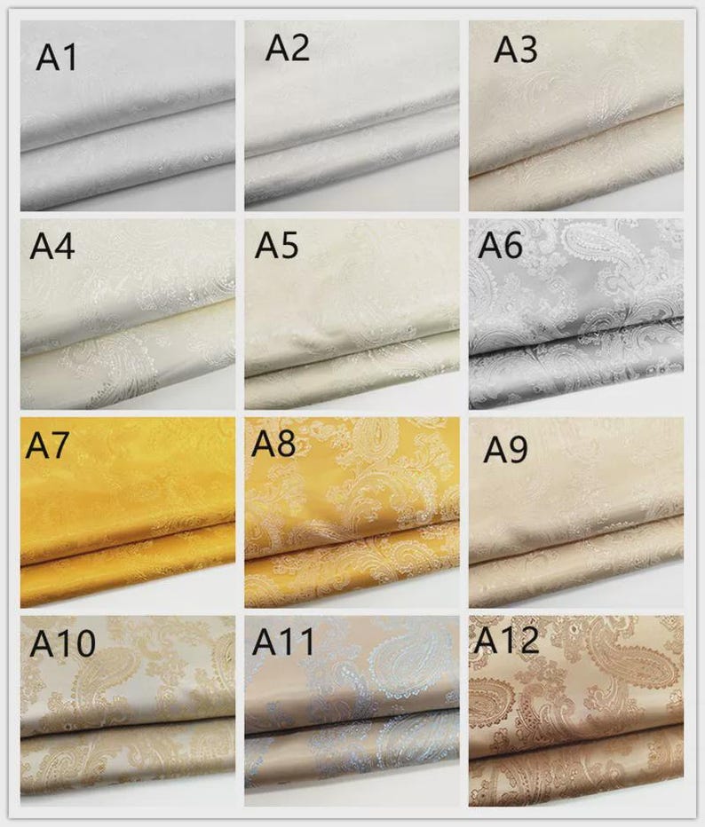 May include: A collection of fabric swatches in various colors, including silver, cream, gold, and beige. Each swatch displays a paisley pattern. The fabrics are neatly folded, showcasing their texture and design. The image is well-lit, highlighting the different shades and patterns.