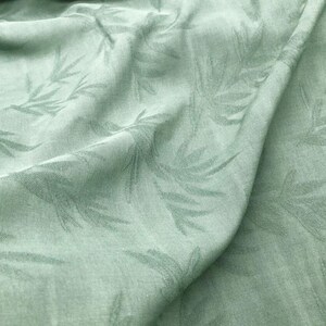 May include: A close-up of a sage green fabric with a subtle embossed leaf pattern. The fabric is soft and has a slightly textured surface.