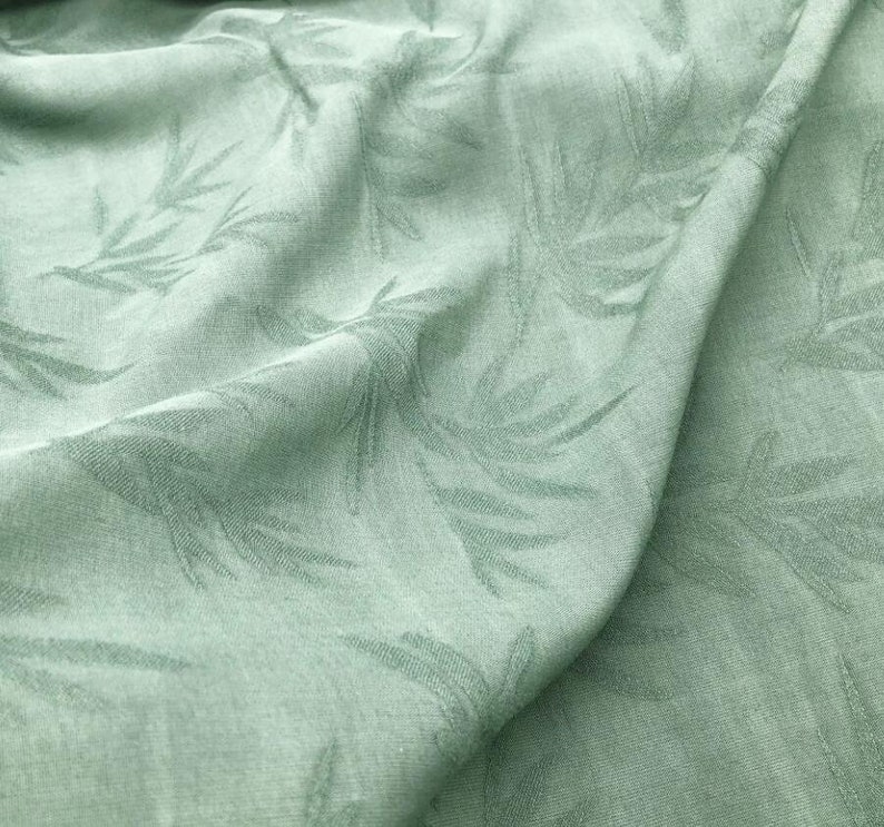 May include: A close-up of a sage green fabric with a subtle embossed leaf pattern. The fabric is soft and has a slightly textured surface.