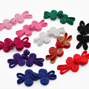 May include: Assortment of ten colorful fabric Chinese knot buttons. The buttons are in various colors, including red, pink, purple, blue, green, white, and black. Each button has a unique design with multiple loops and knots.