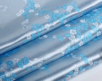 May include: Light blue fabric with a white and blue floral pattern. The fabric is folded in layers, showing the texture and sheen of the material.