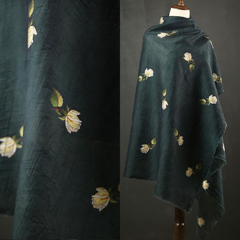 Pu&ograve; includere: Tessuto verde scuro con motivo floreale. Il tessuto &egrave; drappeggiato su un manichino, mostrando fiori bianchi e gialli con foglie verdi. Il tessuto ha un aspetto strutturato.