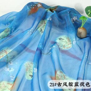 May include: A sheer, flowing fabric in shades of blue, adorned with floral and bird motifs in muted tones of green, orange, and white. The fabric is draped, creating soft folds and shadows. The text "21#" and Chinese characters are visible.