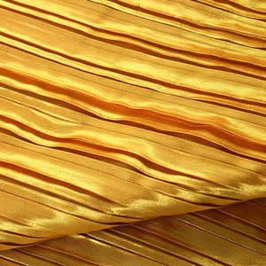 May include: A close-up of a gold pleated fabric. The fabric has a smooth, shiny surface and is folded in a wavy pattern.