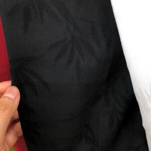 May include: Black fabric with a subtle embossed pattern of leaves. The fabric has a smooth, silky texture.