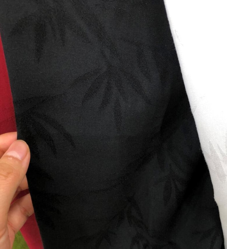 May include: Black fabric with a subtle embossed pattern of leaves. The fabric has a smooth, silky texture.
