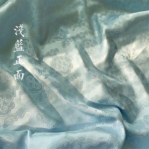 May include: A light blue fabric featuring a repeating woven pattern of stylized clouds. The material has a smooth, satin-like sheen with visible folds and drapes. The Chinese characters 浅藍正面 are printed vertically in white on the left side.