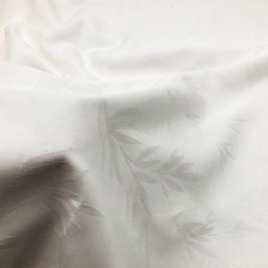 May include: White linen tablecloth with a subtle embossed leaf pattern. The fabric is smooth and has a slight sheen.