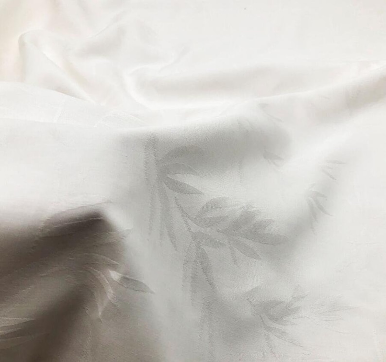 May include: White linen tablecloth with a subtle embossed leaf pattern. The fabric is smooth and has a slight sheen.