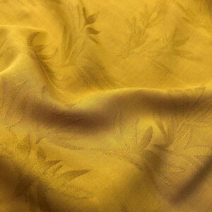 May include: A close-up of a yellow fabric with a subtle embossed leaf pattern. The fabric is soft and has a slightly textured surface.